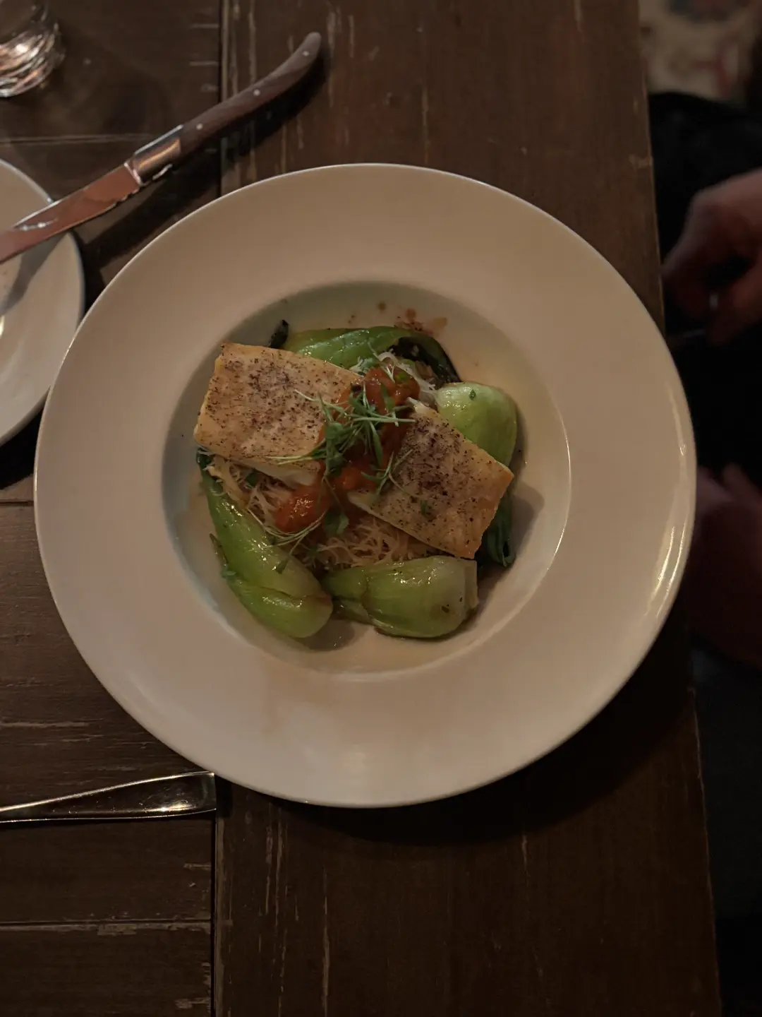 Plated dish with seasoned tofu, snow peas, and garnish served on white plate with knife and fork on dark wooden table