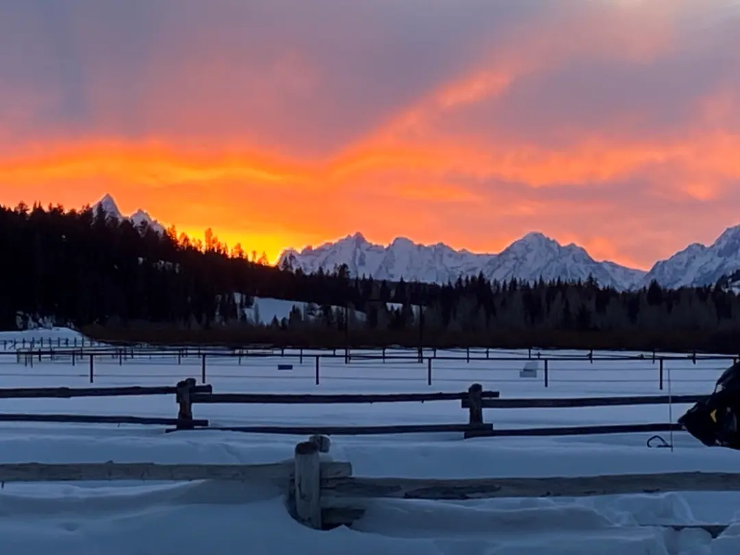 Snow-covered mountain landscape at sunset with wooden fence in foreground and snow-capped peaks of Continental Divide in b...
