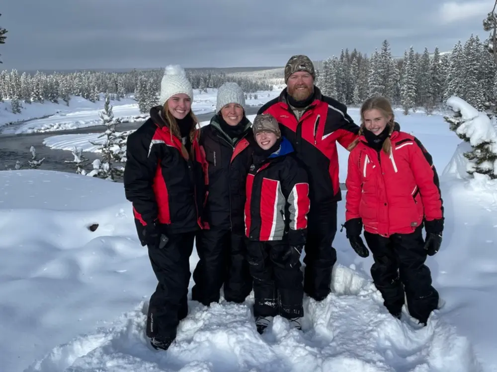 Family of five in winter gear posing in deep snow with snow-covered evergreen forest and river in background during Yellow...